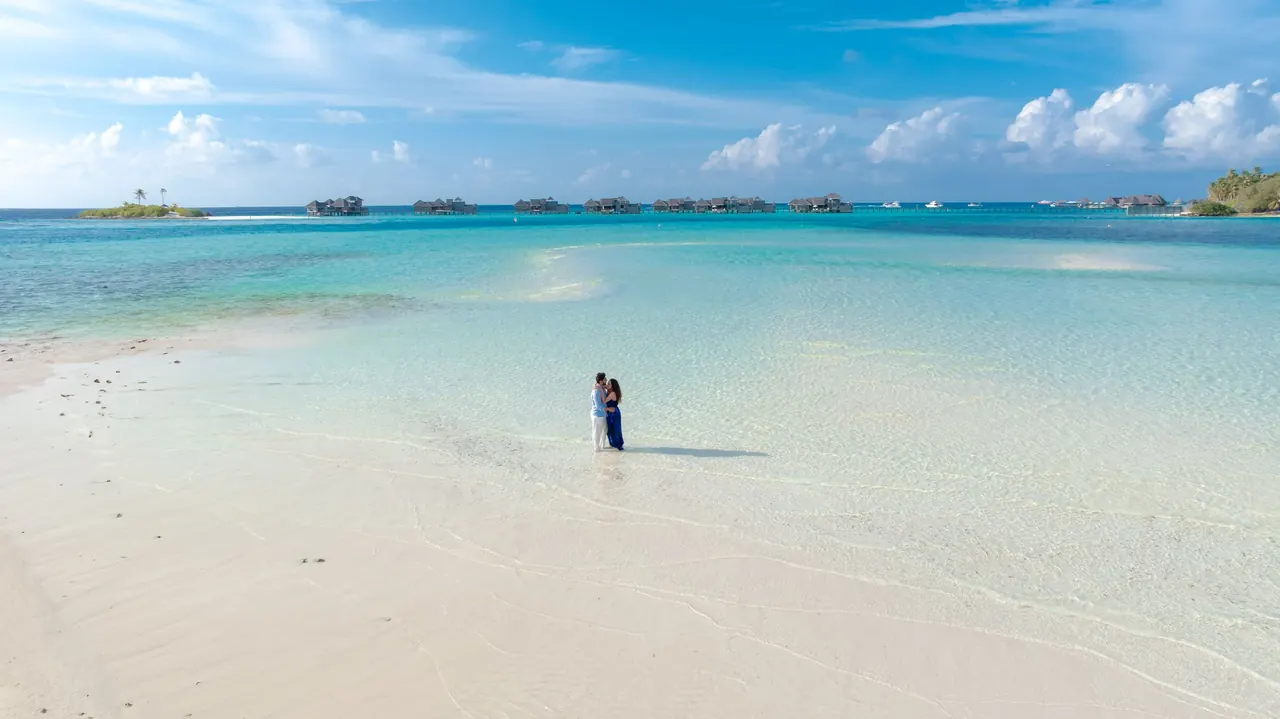 Couple standing on a white sand sandbank beside a turquoise Maldives lagoon
