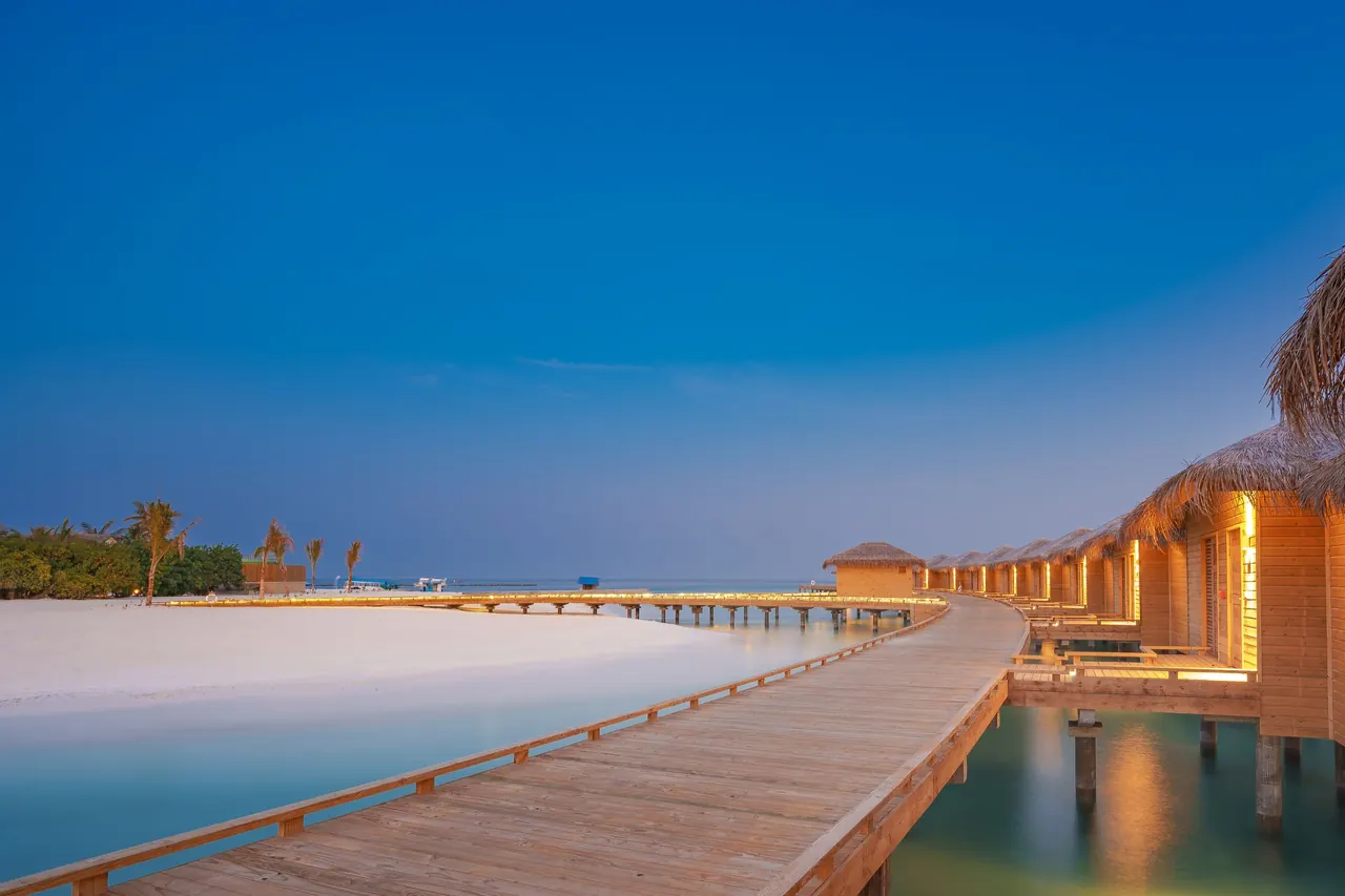 Wooden jetty leading to thatched overwater villas in the Maldives at dusk